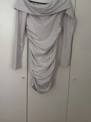 Vit långärmad omlottklänning - Trendig vit klänning med långa ärmar och omlottkrage. Klänningen har draperad effekt längs sidorna och en smickrande, figurnära passform. Perfekt för dig som gillar stilrena och moderna plagg.