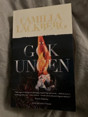Gökungen av Camilla Läckberg - Säljer boken 'Gökungen' av Camilla Läckberg. Omslaget är svart med en eldslåga och text i vitt och guld. Perfekt för dig som gillar spännande och mörka deckare. Mjukt omslag, svensk text. Man behöver inte ha läst de tidigare böckerna för att hänga med enligt mig. 