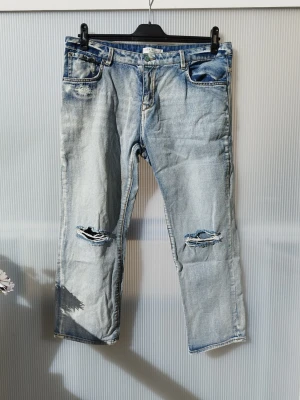 Ljusblå slitna jeans från Denim Hunter - Säljer ett par ljusblå jeans från Lindex med raka ben och slitningar på knäna. Jeansen har klassisk femficksmodell, normal midja och är tillverkade i denim. Perfekta för en avslappnad och trendig look. Storlek 32/32.