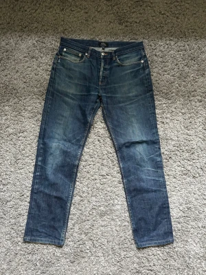 Blå raka jeans från APC - Säljer ett par klassiska blå jeans från APC med raka ben och fem fickor. Jeansen har en snygg tvätt med slitningar och kontrastsömmar. Perfekta till en avslappnad stil och passar till det mesta i garderoben. OBS! upsydda 4-5cm