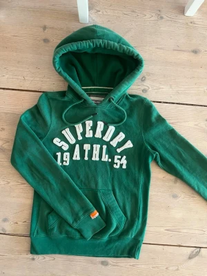 Superdry Hoodie - Säljer en grön hoodie från Superdry. Hoodien är i storlek S men passar mindre. Väldigt bra skick och klassisk passform, perfekt för sommaren. Skriv vid minsta fundering!🙌🙌🤗