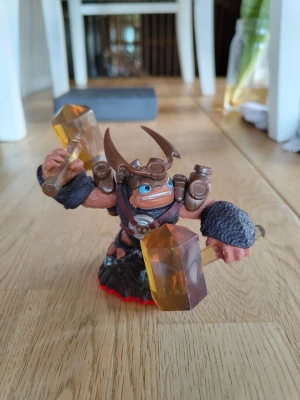Skylanders Trap Team – Wallop (Trap Master) | Jordelement - Säljer en Wallop-figur till Skylanders Trap Team! Han är en kraftfull Trap Master från jordelementet (Earth element) och är känd för sina två gigantiska bärnstensfärgade hammare.  Ett måste för dig som vill låsa upp nya områden i spelet eller komplettera din Skylanders-samling!  Mycket fint begagnat skick. Hel och ren, inga trasiga delar (se bilder för detaljer).  Fungerar till Skylanders Trap Team (och senare spel som SuperChargers och Imaginators). Fungerar oavsett konsol!