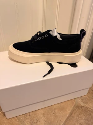 Svarta Eytys mother  - Stilrena svarta sneakers från Eytys med kraftig vit sula och lila hälflik. Skorna är i svart mocka. 