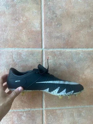 Nike Mercurial fotbollsskor svart/vit - Säljer ett par Nike Mercurial fotbollsskor i svart med vita detaljer och sicksackmönster på sidan. Skorna har snörning, låg profil och dobbar i plast för bra grepp på planen. Tillverkade i syntetmaterial med NIKESKIN-teknologi för extra känsla och kontroll.