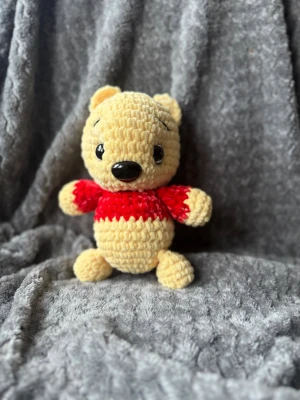 Gul virkad nallebjörn med röd tröja - Söt handvirkad nallebjörn i mjukt gult garn med stora svarta ögon och nos. Nallen har en röd tröja och är perfekt som dekoration eller present. 