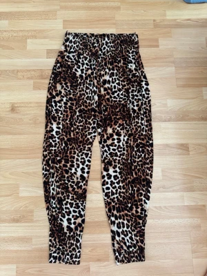 Haremsbyxor med leopardmönster - Säljer ett par mjuka och sköna byxor med leopardmönster i brunt, svart och beige. Byxorna har resår i midjan och vid bensluten för en avslappnad passform. Perfekta för dig som vill sticka ut med ett djurmönstrat plagg. Använd en gång.