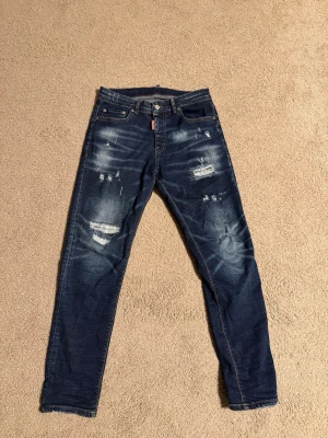 dsquared jeans  - Säljer ett par mörkblå jeans med skinny fit och slitna detaljer på både fram- och baksida. Jeansen har klassisk femficksmodell, dragkedja och knapp i midjan samt kontrastsömmar. Perfekta för en avslappnad och trendig look.