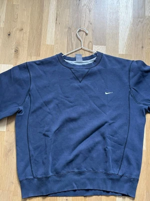 Blå sweatshirt från Nike - Säljer en klassisk mörkblå sweatshirt från Nike med diskret logga på bröstet. Tröjan har rund halsringning och ribbade muddar vid ärmslut och nederkant. Perfekt för en avslappnad och sportig look.