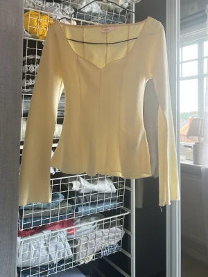 Ljusgul långärmad topp Gina Tricot - Supersnygg ljusgul topp från Gina Tricot med lång ärm och en unik sweetheart-ringning. Toppen har en lätt utsvängd nederkant och är tillverkad i ett mjukt, stretchigt material som sitter bekvämt på kroppen. Perfekt för dig som vill ha en stilren men ändå trendig look.