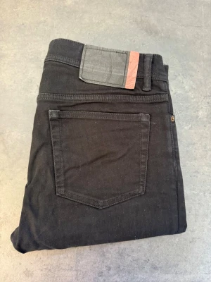 Svarta Slim jeans från Acne Studio, stl 33/34 - Säljer ett par svarta Slim jeans från Acne Studios. Klassisk femficksmodell med smal passform och normal midja. Jeansen har en diskret logga på bakfickan och är tillverkade i stretchigt bomullsmaterial för extra komfort.