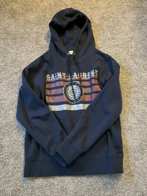Mörkblå Saint Laurent hoodie - Säljer en stilren mörkblå hoodie från Saint Laurent i storlek S.