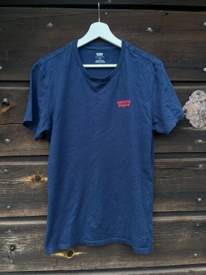 Marinblå t-shirt från Levi's - Snygg marinblå t-shirt från Levi's med klassisk röd logga på bröstet. T-shirten har rund halsringning och korta ärmar. Tillverkad i mjuk bomull som känns skön mot huden. Perfekt till jeans eller shorts för en enkel och clean look. Slim modell