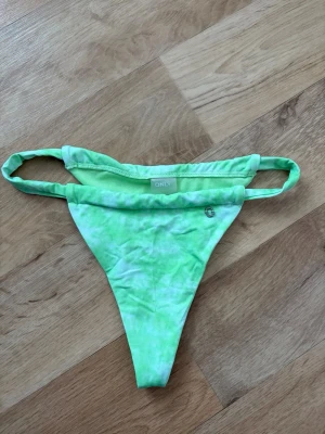 Grön bikiniunderdel från ONLY - Snygg grön bikiniunderdel från ONLY i en fräsch batikliknande nyans. Modellen har smala sidoband och en liten metalllogga framtill. Perfekt för strandhäng och pooldagar! Helt oanvänd, nypris 199kr.