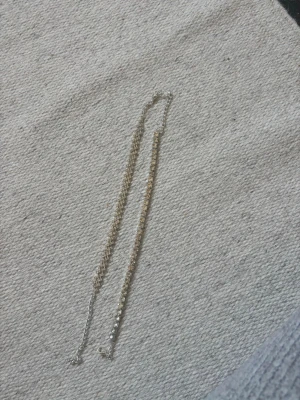Två glittriga armband/ fotlänkar - Säljer två snygga armband/ fotlänkar i silverfärg med gnistrande stenar. Ena armbandet har en klassisk rad av stora, runda stenar medan det andra har ett mer detaljerat mönster med mindre stenar i ett kryssmönster. Perfekta för att ge din outfit extra bling.