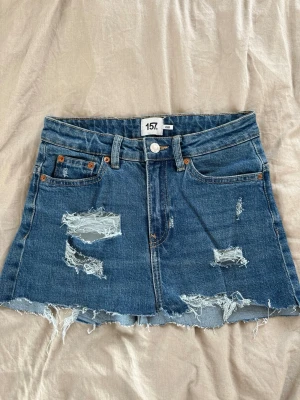 Blå jeanskjol med slitningar från 157 - Egenklippt jeanskjol av ett par byxor från lager 157. Super snygg och cool till sommaren.