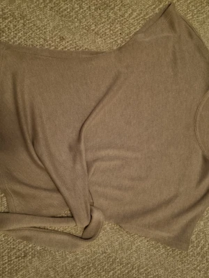 Beige stickad topp med knytband - Säljer en beige stickad topp med knytband i midjan. Tröjan har en enkel, stilren design och är tillverkad i mjukt, tunt stickat material. Perfekt för lager på lager och passar till många olika outfits.