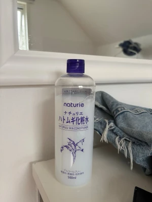 Naturie Hatomugi Skin Conditioner - En stor flaska toner från Naturie med Hatomugi-extrakt (pärlkorn). Flaskan är genomskinlig med lila lock och lila text, rymmer 500 ml och har en enkel, stilren design. Perfekt för att återfukta huden och ge en fräsch känsla.