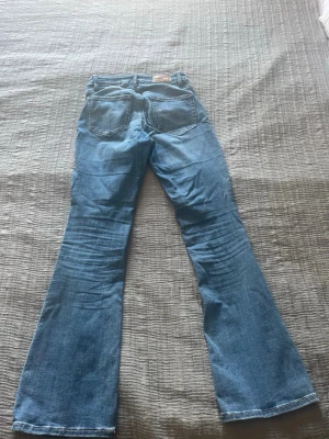 Blå utsvängda jeans med fickor - Säljer ett par ljusblå jeans med utsvängda ben och klassiska fem fickor. Jeansen har en snygg tvätt och markerade sömmar. Perfekta för dig som gillar retrostil och vill sticka ut lite extra.