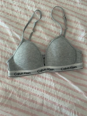 Grå Calvin Klein bralette - Snygg grå bralette från Calvin Klein med justerbara axelband och elastisk logoresår under bysten. Mjuk och bekväm modell utan bygel, perfekt för en avslappnad stil. Tillverkad i stretchigt bomullsmaterial. 