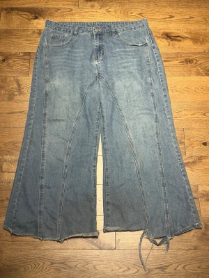 Blåa vida jeans med rå kant - Ett par ljusblå jeans med supervid passform och rå, fransig kant längst ner. Jeansen har klassiska fem fickor och hög midja. Materialet är denim i bomull och benen är extra utsvängda för en retrovibe.