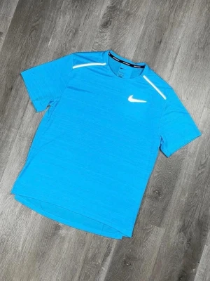 Nike träningströja  - Snygg blå kortärmad träningströja från Nike med logga på bröstet och detaljer vid axlarna. Tillverkad i ett lätt och snabbtorkande material som passar perfekt till träning och sportaktiviteter.