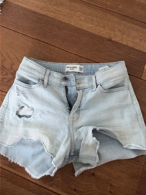 Ljusblå denimshorts från Abercrombie - Säljer ett par ljusblå denimshorts från Abercrombie & Fitch. De är barn storlek 13/14 men passar som en XS. De är i bra skick men har några små fläckar här och där som man ser på bilden, men inget som syns jätte tydligt. 