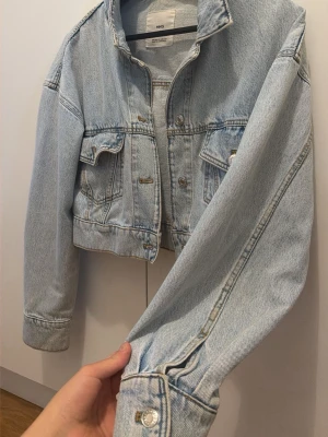 Ljusblå cropped jeansjacka från MNG - Trendig ljusblå jeansjacka från MNG med croppad passform. Klassisk krage, två bröstfickor med knappar och silverfärgade detaljer. Perfekt för att lyfta vilken outfit som helst med en avslappnad vibe.