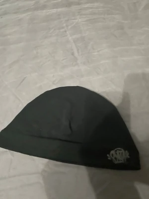 Syns world mössa - En stilren svart mössa från syna world med en broderad vit logga framtill. Tillverkad i mjukt och stretchigt material som sitter skönt på huvudet. Perfekt för att hålla värmen under kyliga dagar och passar till de flesta outfits.