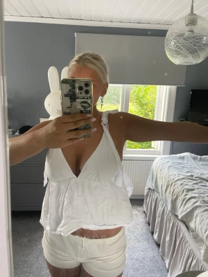 Vitt loungewear-set med topp och shorts - Säljer ett vitt loungewear-set med en luftig topp med knytband på axlarna och djup urringning samt matchande shorts med resår i midjan. Perfekt för chill dagar hemma eller mysiga kvällar. Materialet känns lätt och bekvämt mot huden.