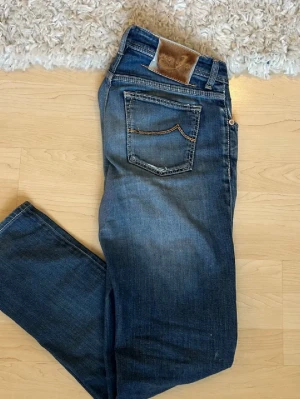 Jacob cohën jeans - Snygga blå jeans från Jacob Cohen med klassisk femfik. Jeansen har en lätt tvättad look, synliga slitningar och en broderad J på myntfickan. Tillverkade i denim med skinnpatch bak i midjan. Storlek 33