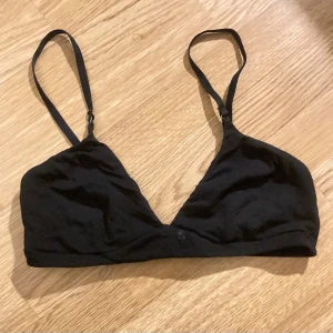 Svart triangelformad bralette - Säljer en stilren svart bralette i storlek L, med triangelformade kupor och justerbara axelband. Bh:n har hakknäppning bak som en vanlig bh och är tillverkad i ett mjukt tyg, perfekt om man vill ha en bekväm och skön bh. Är köpt på Lindex. Säljes pga för liten🤩☺️