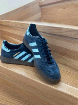 Adidas Spezial blå sneakers - Snygga Adidas Spezial sneakers i blå mocka med ljusblå ränder och detaljer. Klassisk låg modell med gummisula och svart snörning. Perfekta för dig som gillar retrostil och streetwear.
