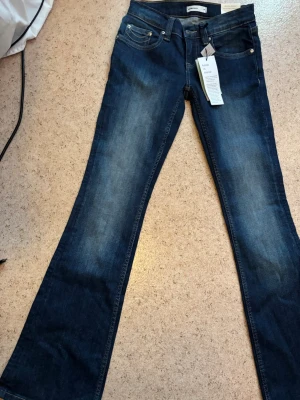 Mörkblå bootcut jeans ultra low - Säljer ett par mörkblå bootcut jeans med ultra låg midja. Jeansen har klassisk femficksdesign, snygga slitningar och är tillverkade i stretchig denim för skön passform. Perfekta för dig som gillar en avslappnad men trendig look. De är helt nya med prislapp på