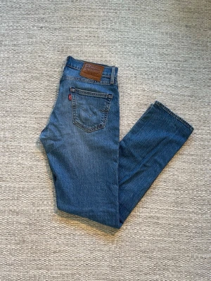 Blå raka jeans från Levi's - Klassiska blå jeans från Levi's med rak passform och femficksdesign. Jeansen har en brun läderpatch bak i midjan och den ikoniska röda Levi's-taggen på bakfickan. Tillverkade i slitstarkt denimtyg som ger en tidlös look.