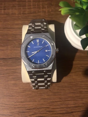 Audemars Piguet Royal Oak  - Snygg Audemars Piguet Royal Oak klocka med blå urtavla och datumvisning. Klockan har en ikonisk åttakantig boett och länkarmband i silverfärgat stål. Perfekt accessoar för dig som gillar exklusiv och tidlös design. Priset kan diskuteras!