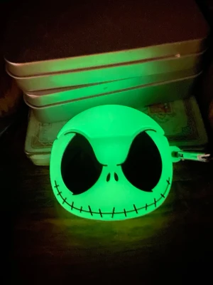 Airpods Glow in the dark Jack Skellington skal  - Säljer ett glow in the dark mobilskal i silikon med Jack Skellingtons ansikte från Nightmare Before Christmas. Skalets form är rund och det har en karbinhake för enkel upphängning på väska eller nyckelknippa. Perfekt för dig som gillar unika och nördiga accessoarer.Passar till Airpods 1-2