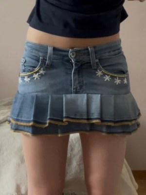 Blå jeanskjol med volang och broderi - En Lågmidjad jeanskjol omsydd från ett par jeans med blomdetaljer. 🌸  Midjemått tvärsöver - 31cm (stretchig) Längd - ca 30cm