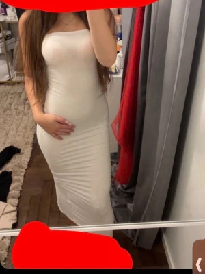 Vit axelbandslös långklänning - Säljer en stilren vit långklänning med axelbandslös design. Klänningen har en tight passform och är perfekt för dig som vill ha en enkel men snygg look. Materialet ser ut att vara mjukt och stretchigt, vilket ger en smickrande siluett.
