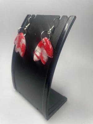 Röda och vita handgjorda örhängen - Unika örhängen i röd och vit färg med abstrakt mönster. De är formade som blad och har en glansig yta. Örhängena är handgjorda i polymerlera och har silvriga krokar. Perfekta för dig som vill sticka ut med färgglada accessoarer.