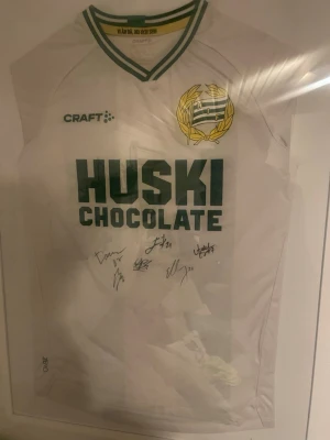 Vit Hammarby fotbollströja Craft signerad - Säljer en vit Hammarby fotbollströja från Craft med gröna detaljer och klubbmärke på bröstet. Tröjan har trycket 'Huski Chocolate' på framsidan och flera autografer av blandannat besara darian bojanic och Edvin kurtulus och nahir besara. Perfekt för dig som älskar fotboll och Hammarby. Kom gärna med bud om inte 1500 funkar pga autografernas värde