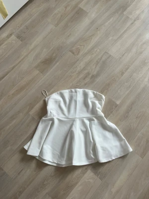 Vit bandeau topp från hm - Säljer en ny oanvänd bandeau topp från hm i storlek M. Toppen är axelbandslös med en lätt utsvängd peplum nedtill och har en enkel, stilren design. Perfekt för sommarens alla tillfällen och lätt att matcha med olika outfits.
