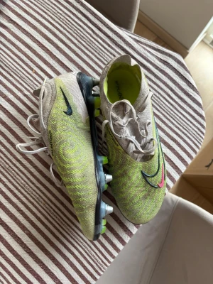 Nike Phantom fotbollsskor lime/beige - Säljer ett par Nike Phantom fotbollsskor i limegrönt och beige med svarta och rosa detaljer. Skorna har snörning, mönstrad ovandel och metall-dobbar för bästa grepp på planen. Storlek 40!