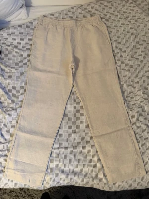Beiga linnebyxor med resårmidja - Säljer ett par beiga linnebyxor med rak passform och resår i midjan. Byxorna har en enkel och stilren design, perfekta för en avslappnad look. Tillverkade i ett lätt och luftigt linnematerial som passar bra till varmare dagar.
