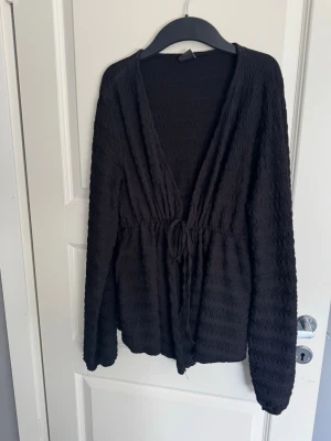 Svart set med strukturmönster - Snyggt svart set med långärmad blus och matchande byxor. Blusen har djup v-ringning, knytband i midjan och ett mjukt, stretchigt tyg med struktur. Byxorna är vida och har samma material och mönster som toppen. De är svarta och mörka, det är bara dåligt ljus. Är man intresserad av endast ett plagg kan man skriva till mig.