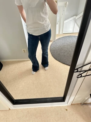 Mörkblå bootcut jeans - Säljer ett par mörkblå bootcut jeans med klassisk femficksdesign och normal midja. Jeansen har en snygg tvätt och lätt utsvängda ben som ger en trendig siluett. Endast provade!