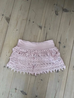 Ljusrosa spetsshorts  - Supersöta ljusrosa shorts med bred midja och flera lager spetsvolanger. Tillverkade i mjuk bomull med lite stretch för extra komfort. Perfekta för varma dagar när du vill ha en romantisk och trendig look.