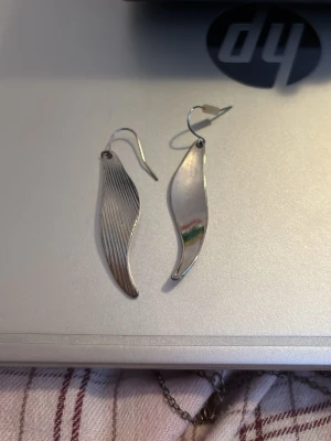 Silvriga vågformade örhängen - Säljer ett par silvriga örhängen i vågformad design. Ena sidan har släta linjer medan det andra har räfflade detaljer. Säljer de pga att jag använder inte silver