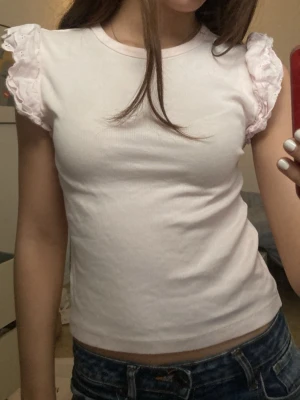 Ljusrosa topp med volangärmar - Supersöt ljusrosa topp med korta volangärmar i broderad bomull. Toppen har rund halsringning och är figurnära i modellen. Perfekt att styla med jeans för en chill look. Volangdetaljerna ger en extra touch av romantisk vibe. !Har endast använt ett par gånger hemma! Pris går alltid att diskuteras! Köpte den för 190kr