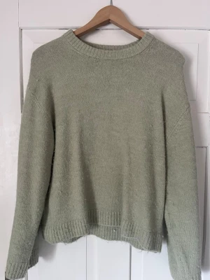 Ljusgrön stickad tröja Gina Tricot - Mysig ljusgrön stickad tröja från Gina Tricot i premiumkvalitet. Tröjan har rund halsringning, långa ärmar och ribbade muddar vid hals, ärmslut och nederkant. Perfekt för kalla dagar och enkel att matcha med olika outfits. Stor i storleken. 