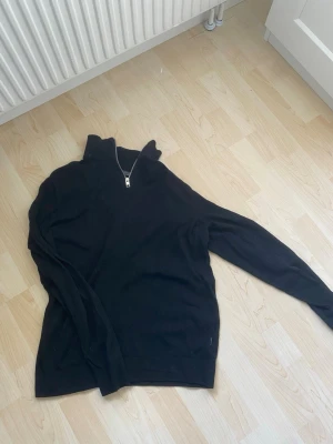 Svart halvzip tröja Jack & Jones - Snygg svart tröja från Jack & Jones med halv dragkedja och hög krage. Perfekt för lager på lager och enkel att matcha med olika outfits. Tillverkad i mjukt material och har långa ärmar.